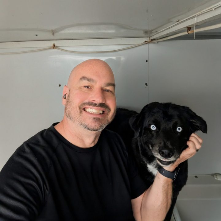 Paul Nickerson smiling next to Kai, an Australian Shepherd, inside the Hurricane Bath trailer